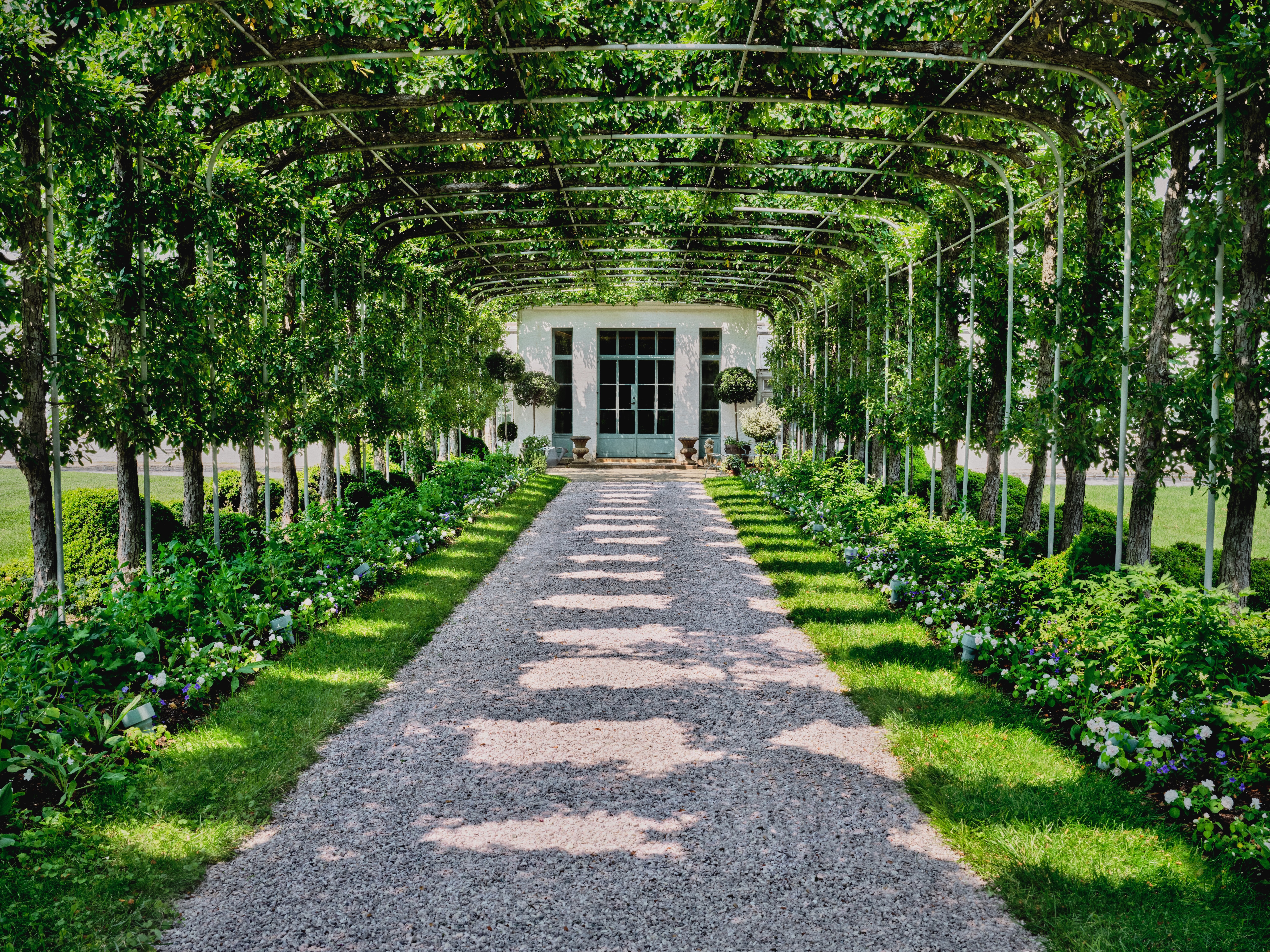 Wide trellis covering a gravel path with turquoise garden doors at one end