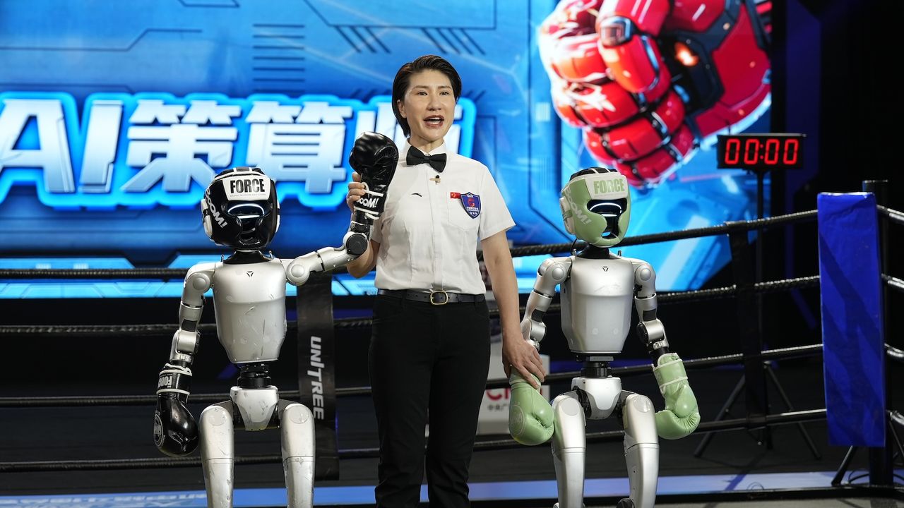 An announcer holds up the hand of a robot that won a boxing match
