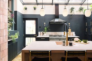 Kitchen with dark blue walls, blue units, pink island and three pendant lights over the worktop