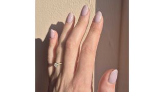 A close-up of Digital Beauty Writer, Naomi Jamieson's lavender milk almond nails/ in front of a pink background