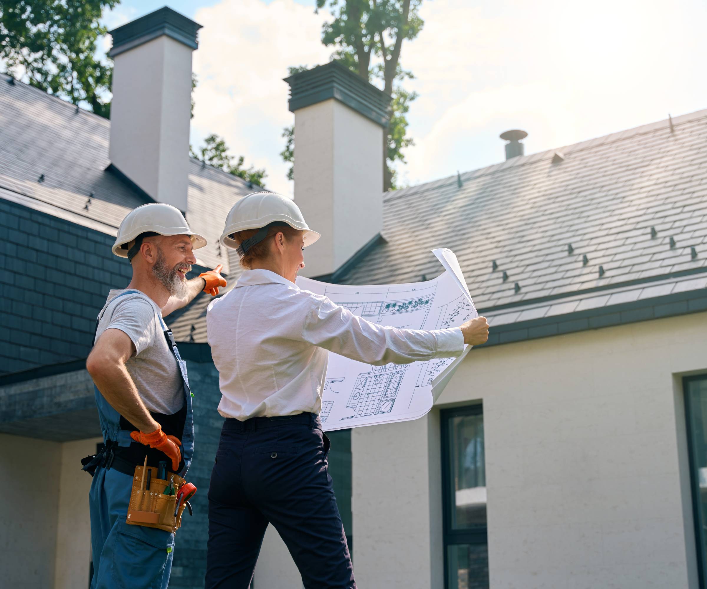 male and female holding set of plans stood outside a modern self build property