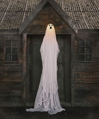 standing ghost with LED lights in front of old wooden cabin