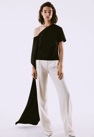 Model wearing one shoulder black top and white pant