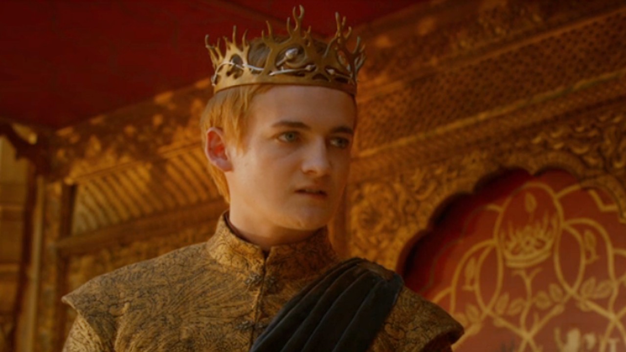 Jack Gleeson as Joffrey standing wearing a crown on Game of Thrones