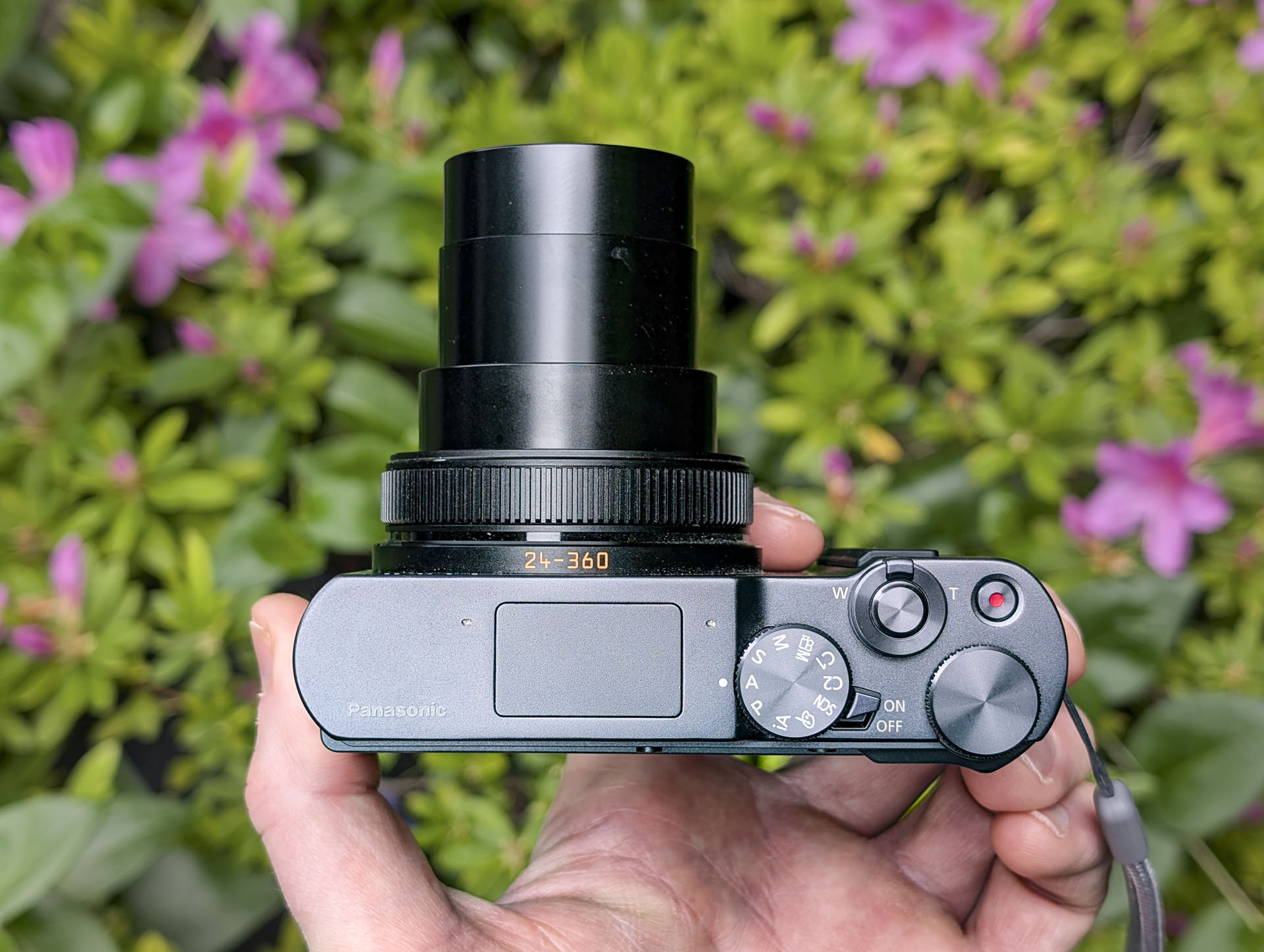 Panasonic Lumix TZ300 compact camera in the hand with a colorful floral backdrop, view of the top and the lens is extended