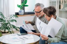A senior couple looks over financial paperwork together in their living room.