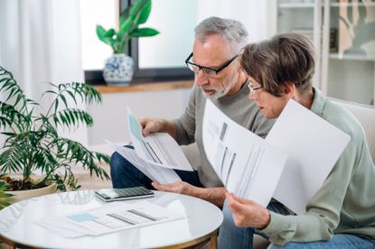 A senior couple looks over financial paperwork together in their living room.