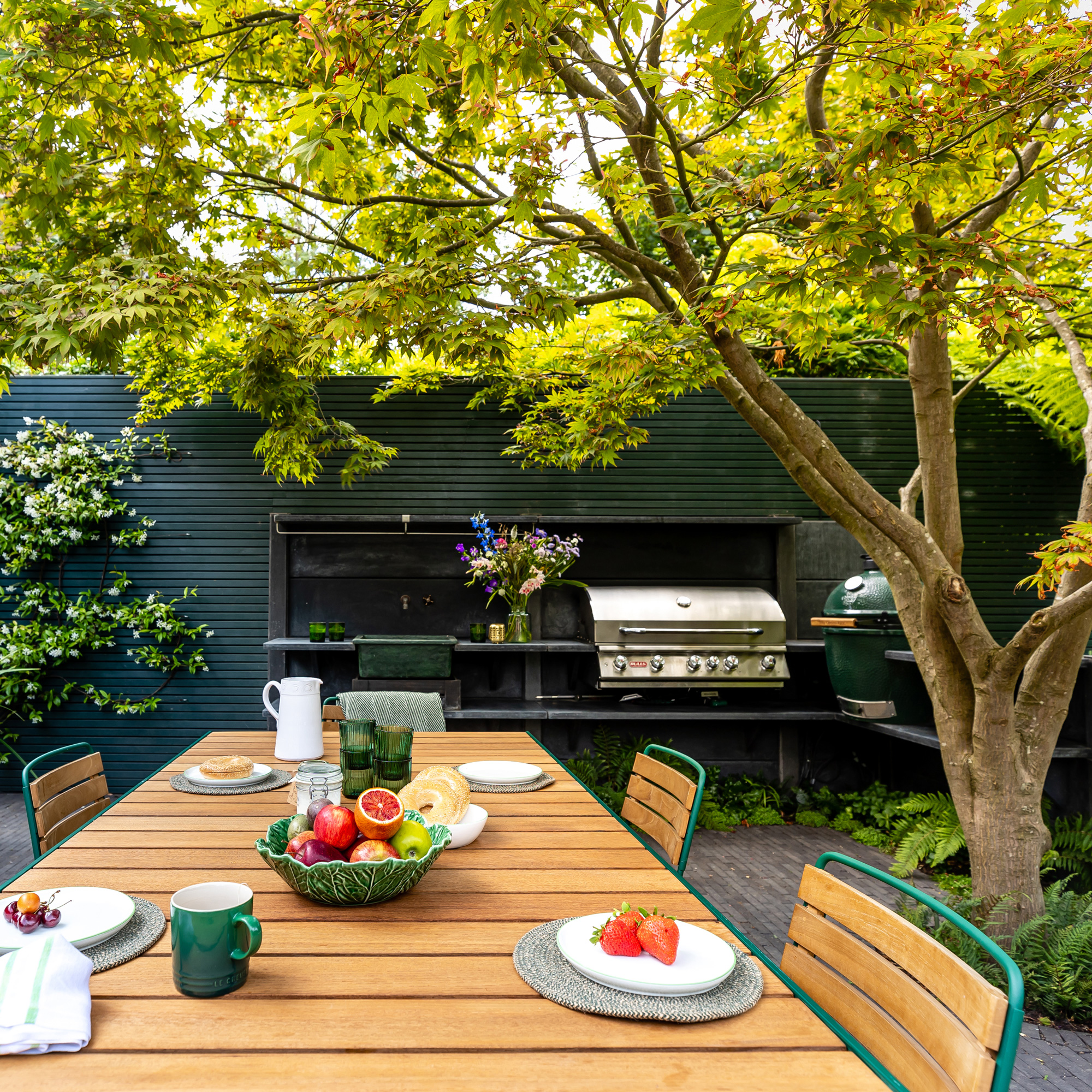 garden makeover with a dining table and chairs, outdoor kitchen with two barbecues and a kitchen sink