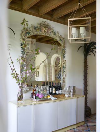 A corner of the home with a large, ornate mirror, a bar cabinet, and a vintage lighting piece hung above it