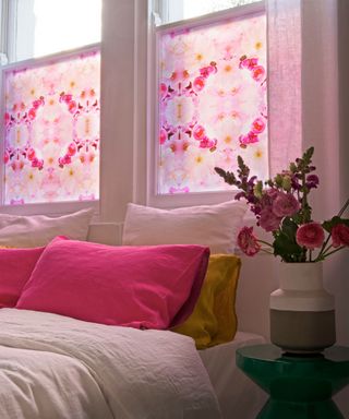 A bed with pink cushions below a window with pink decals