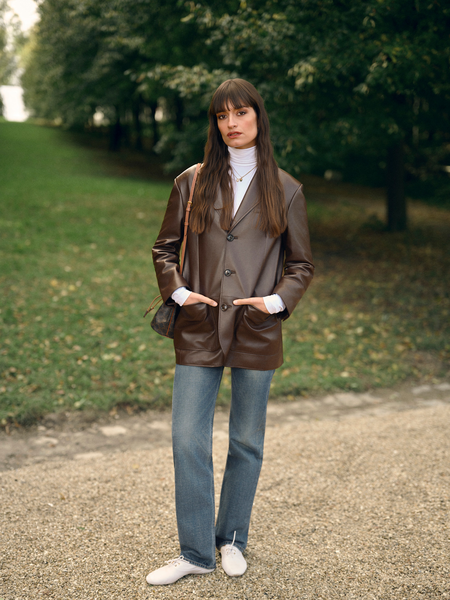 Woman in a brown leather jacket, jeans, and slim white sneakers.