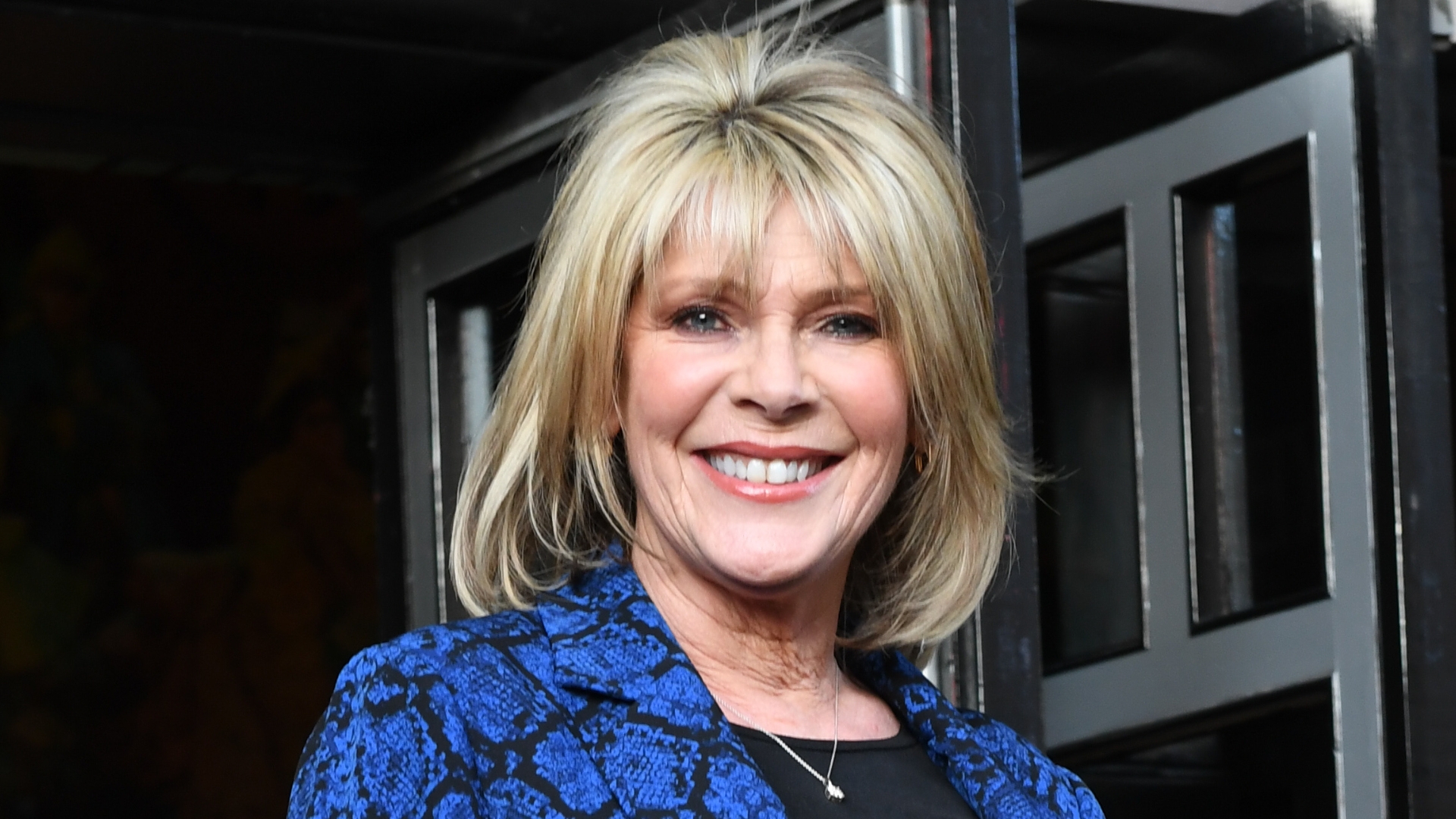 Image of Ruth Langsford smiling with blonde bob with fringe, wearing a black and blue patterned blazer
