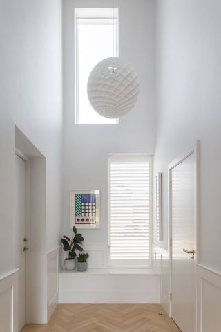 A double height hallway with large white ball light at the centre and a bench in front of a window