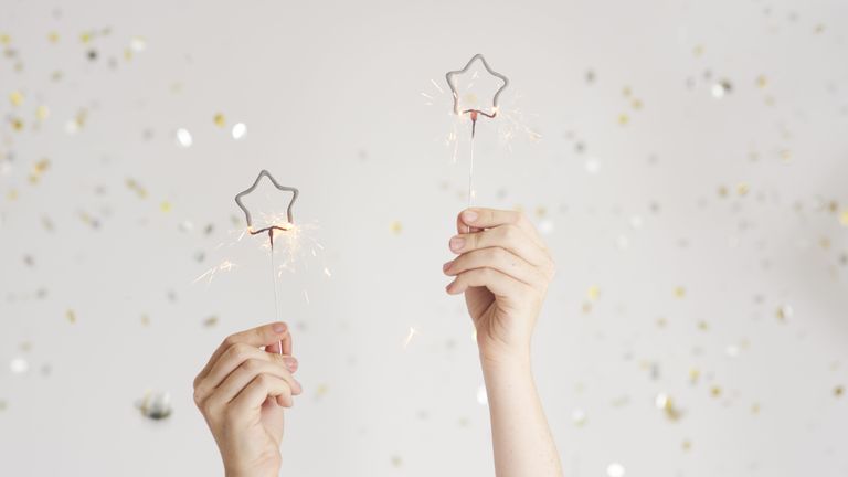 two hands holding sparklers with confetti