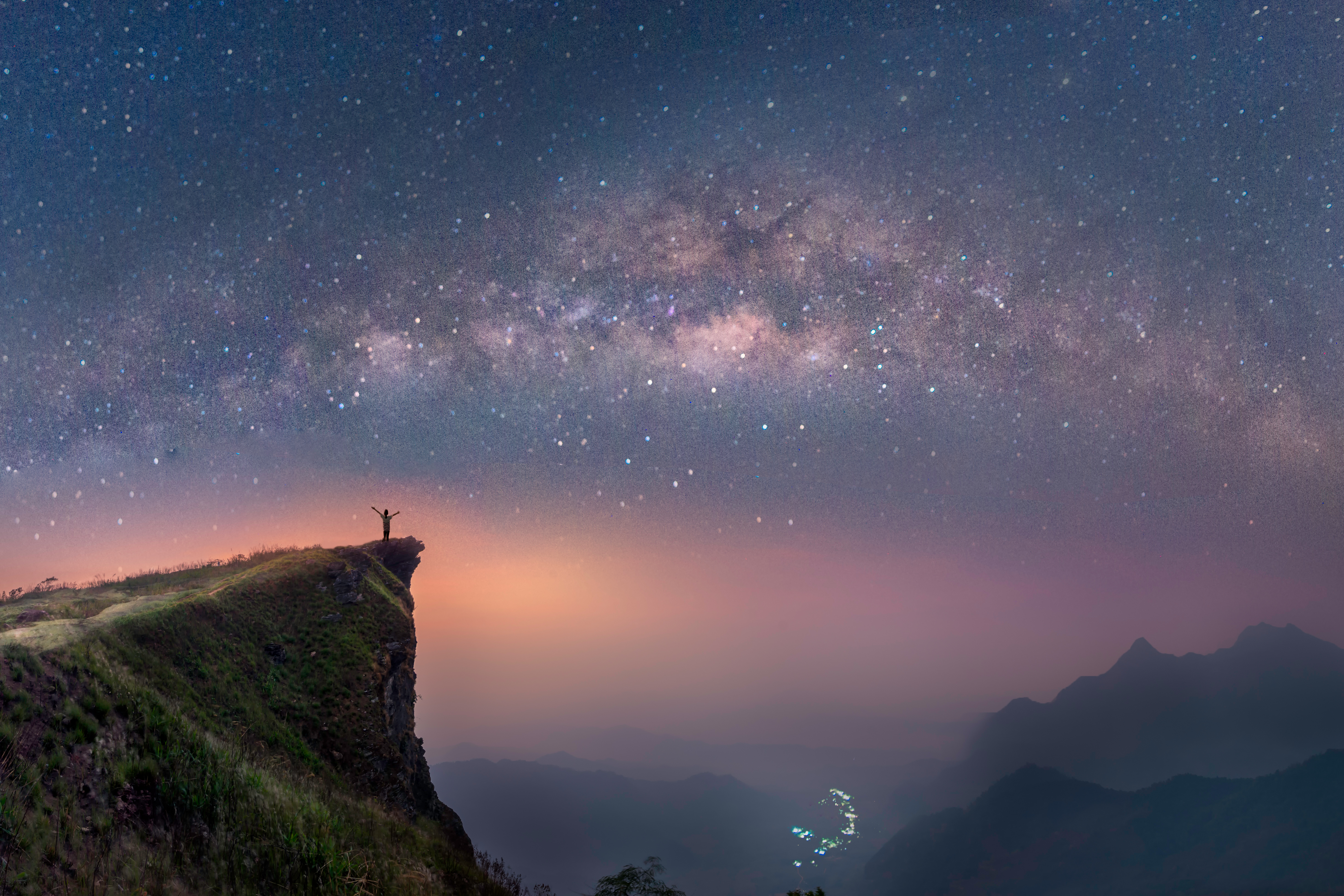 A lone figure standing on a rocky outcrop with the Milky Way visible above them
