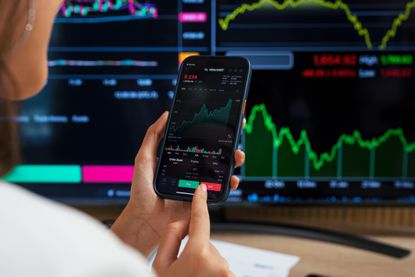 woman looking at stock charts and brokerage account on smartphone and PC