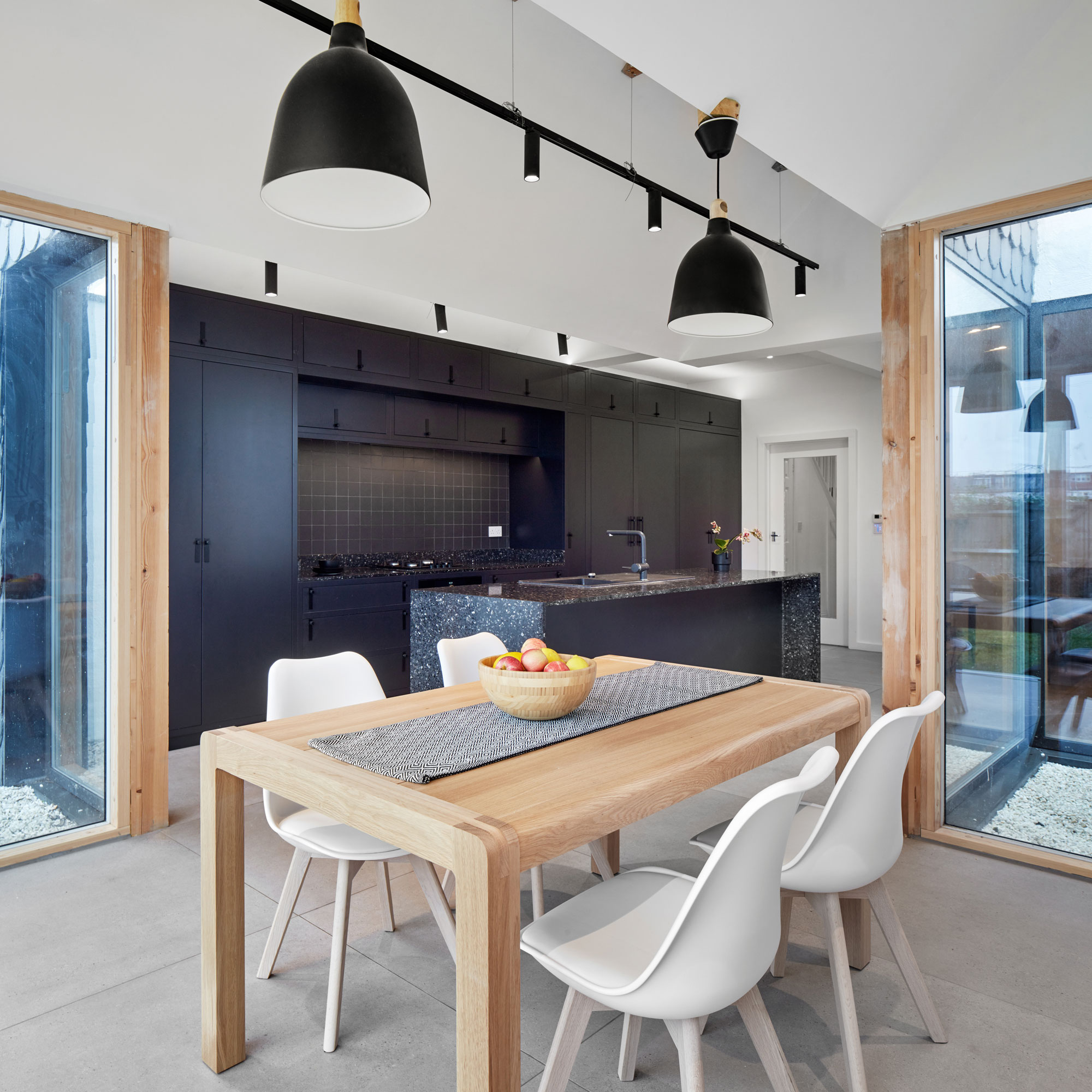 a black kitchen with pale wood dining table and white chairs