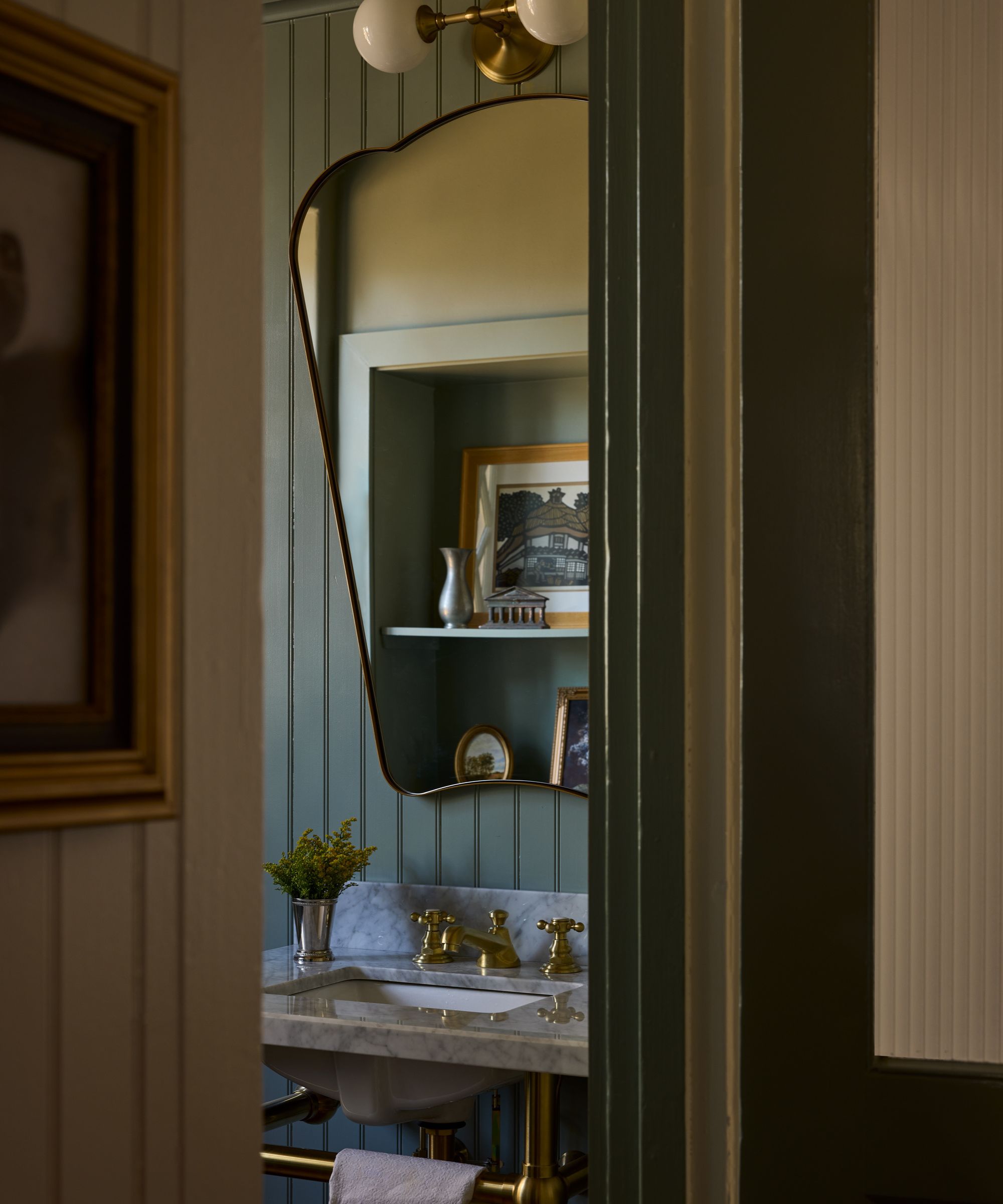 Pale blue paneled bathroom with large mirror, marble sink and gold light above the mirror