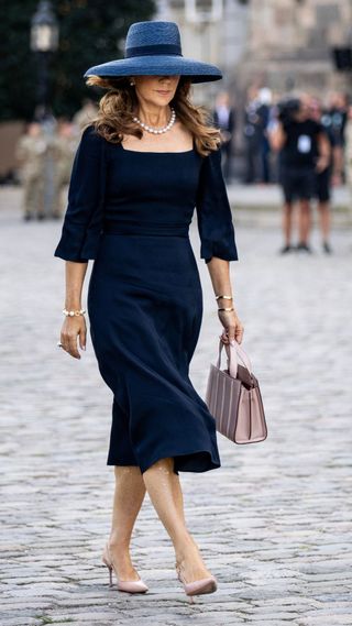 Queen Mary of Denmark wearing a navy dress and statement sun hat