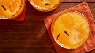 overhead shot of a three cocktail glasses with with orange liquid. clove buds float on top of each