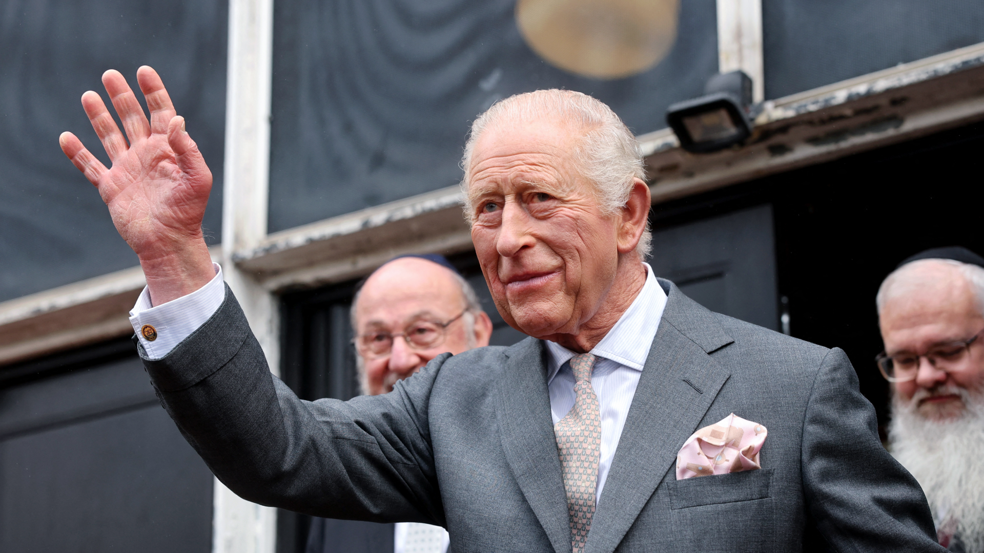 King Charles wearing a gray suit and waving