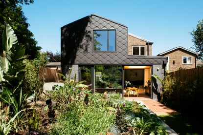 A back view of a double storey home with a garden, brick flooring and a black curved pattern on the house