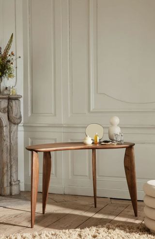 Curvaceous wooden desk, decorated with ornaments, white paneled walls, wooden floor with textured brown rug