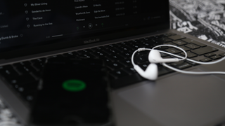 MacBook Air y smartphone ejecutando Spotify con un par de auriculares en el teclado