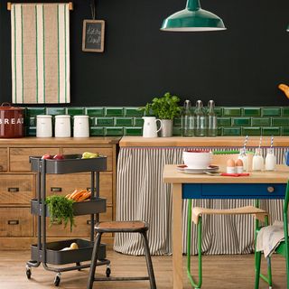 kitchen with black walls and green splashback, with wooden cupboards and table, and a black portable kitchen trolley