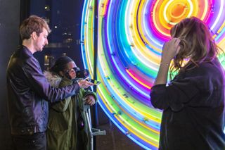 Alastair holds his phone in front of Shana-Rochelle's lens to reflect the neon sign and make a more colourful portrait