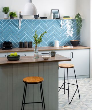 Herringbone kitchen wall tile ideas in blue, in a white kitchen with a gray kitchen island and bar stools.