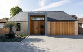 contemporary self-build home with large timber garage doors, an oversized timber front door and a paved driveway
