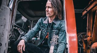 Myles Kennedy poses outdoors by a camper van with his PRS signature guitar that he used to record his new solo album, The Art Of Letting Go