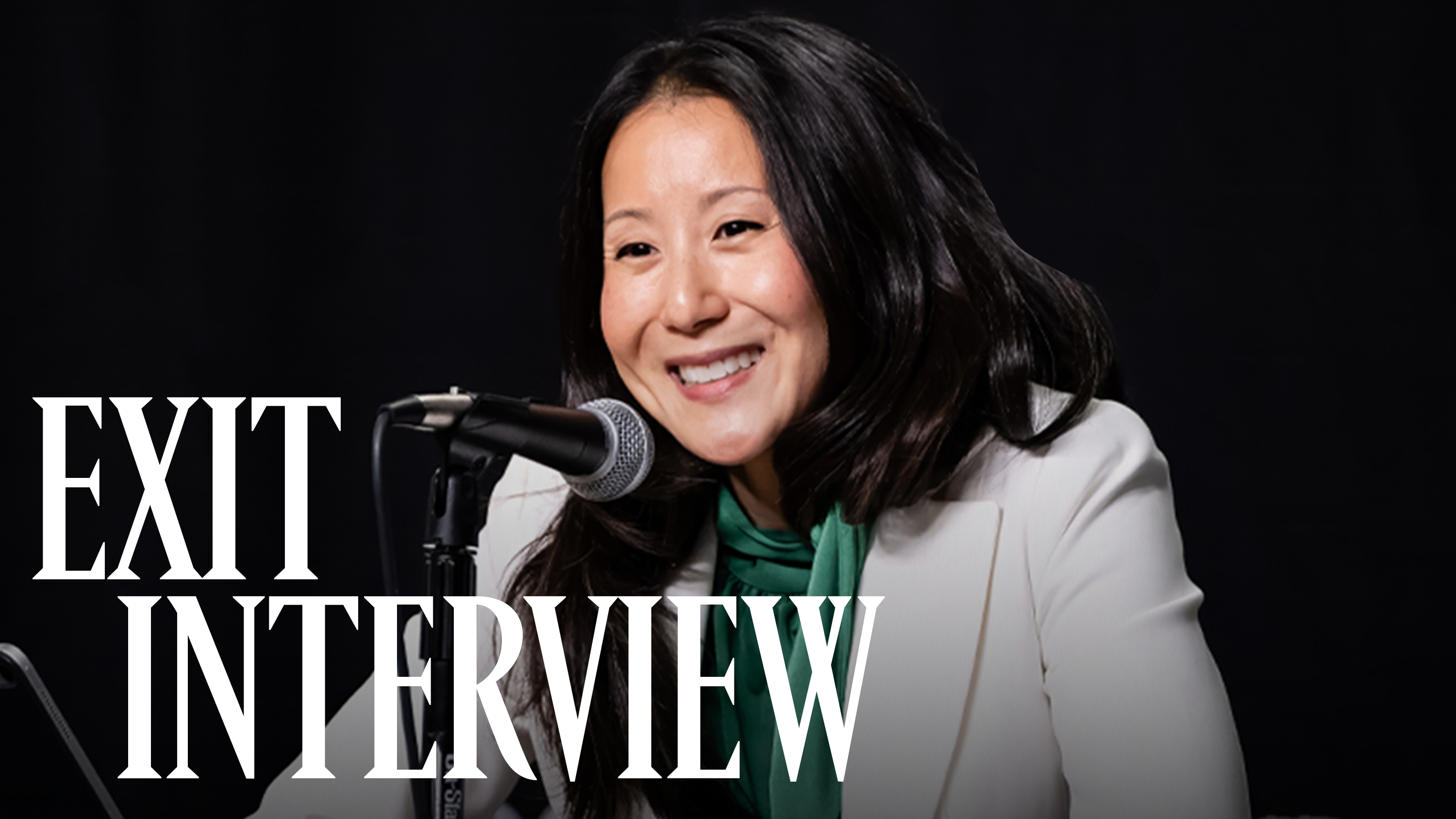 A photo of USA Gymnastics president and CEO Li Li Leung smiling in front of a microphone against a black backdrop.