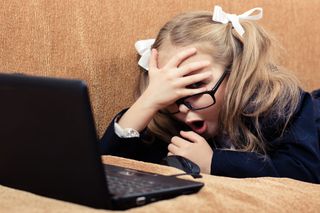 Young girl clamping hand to forehead while looking at laptop
