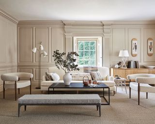All beige living room ideas in a scheme with wall panels, floor lamp, black coffee table and beige sofa and armchairs.