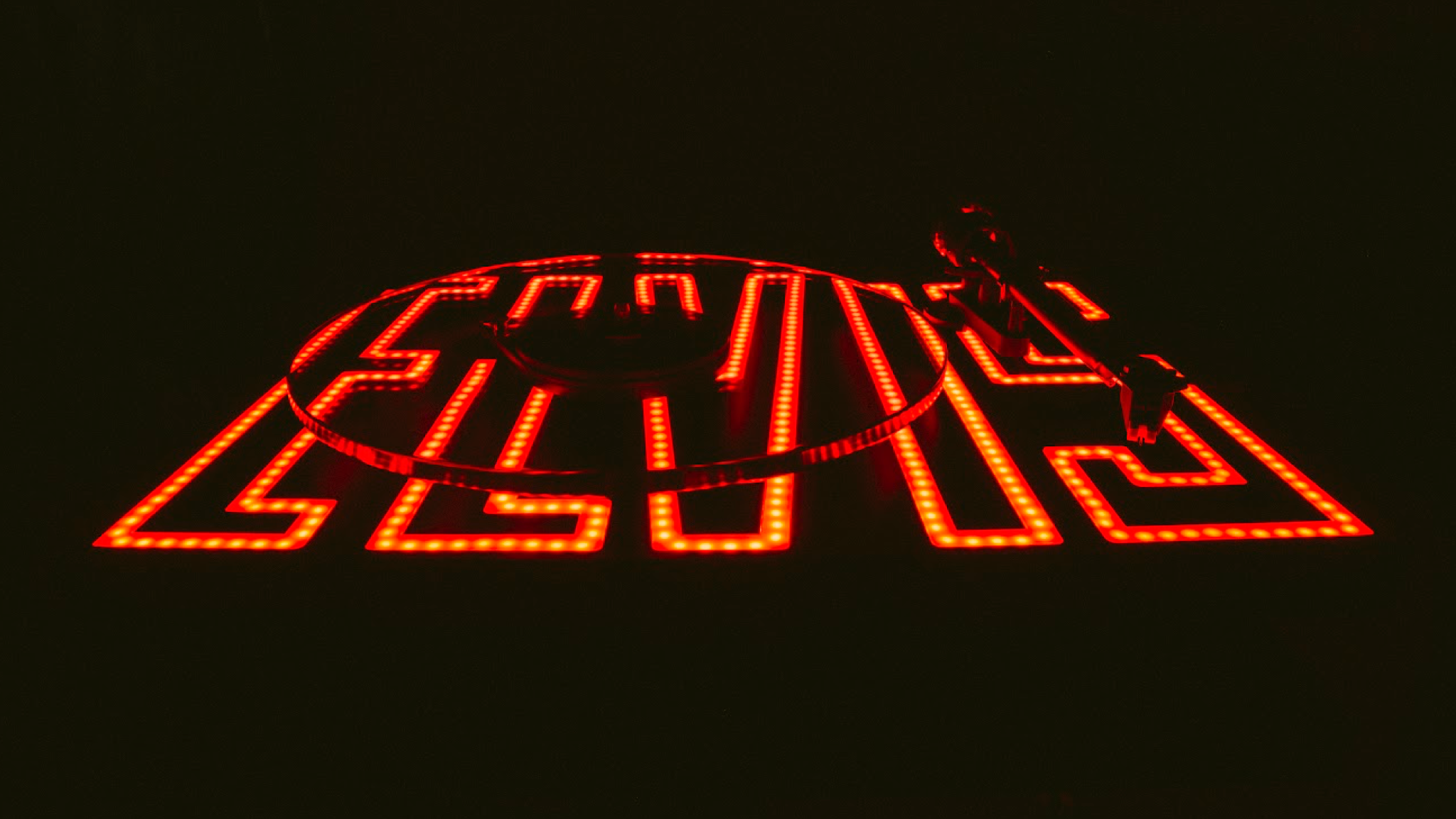 Pro-Ject Elvis Turntable on a black background with the ELVIS logo illuminated in red and orange