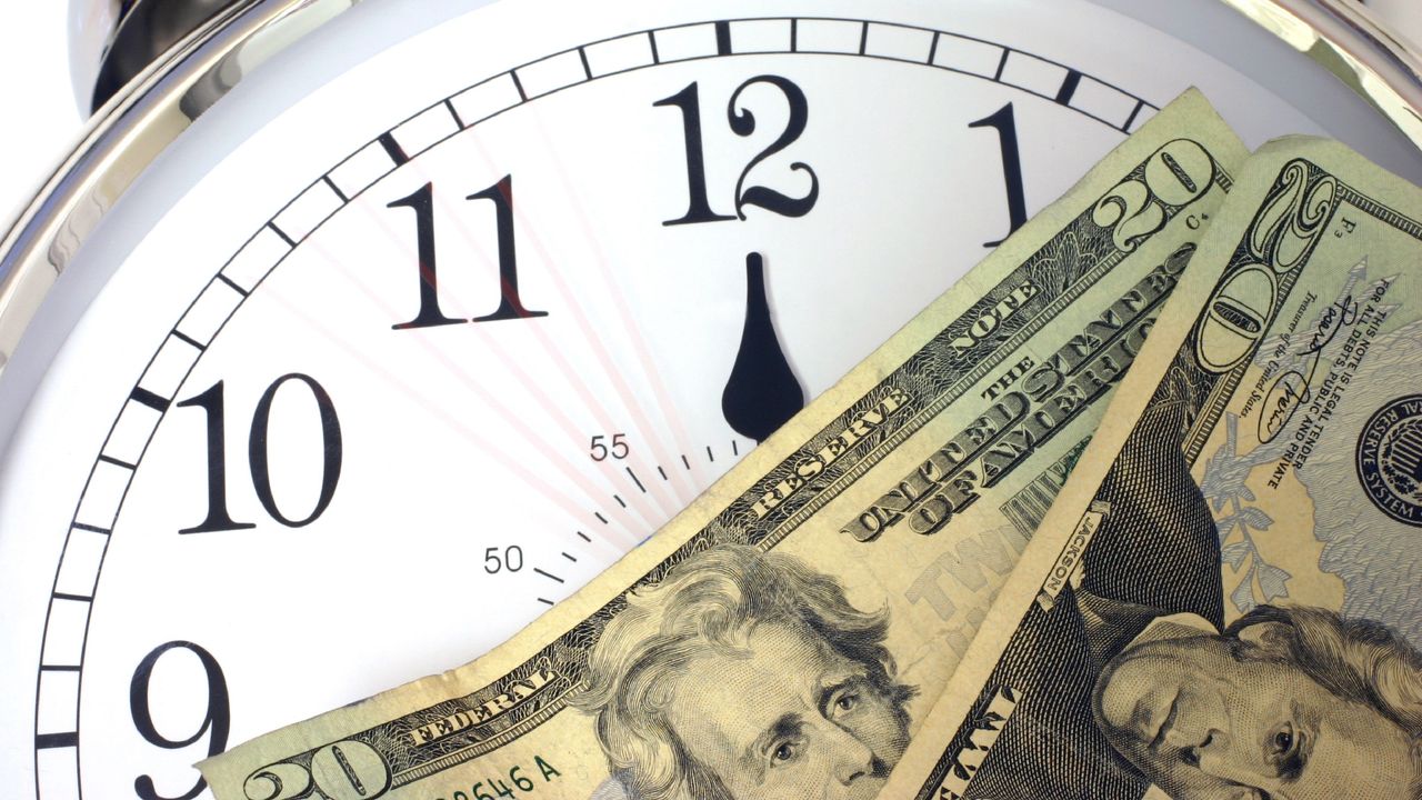 A clock in the background with cash on top of its face.