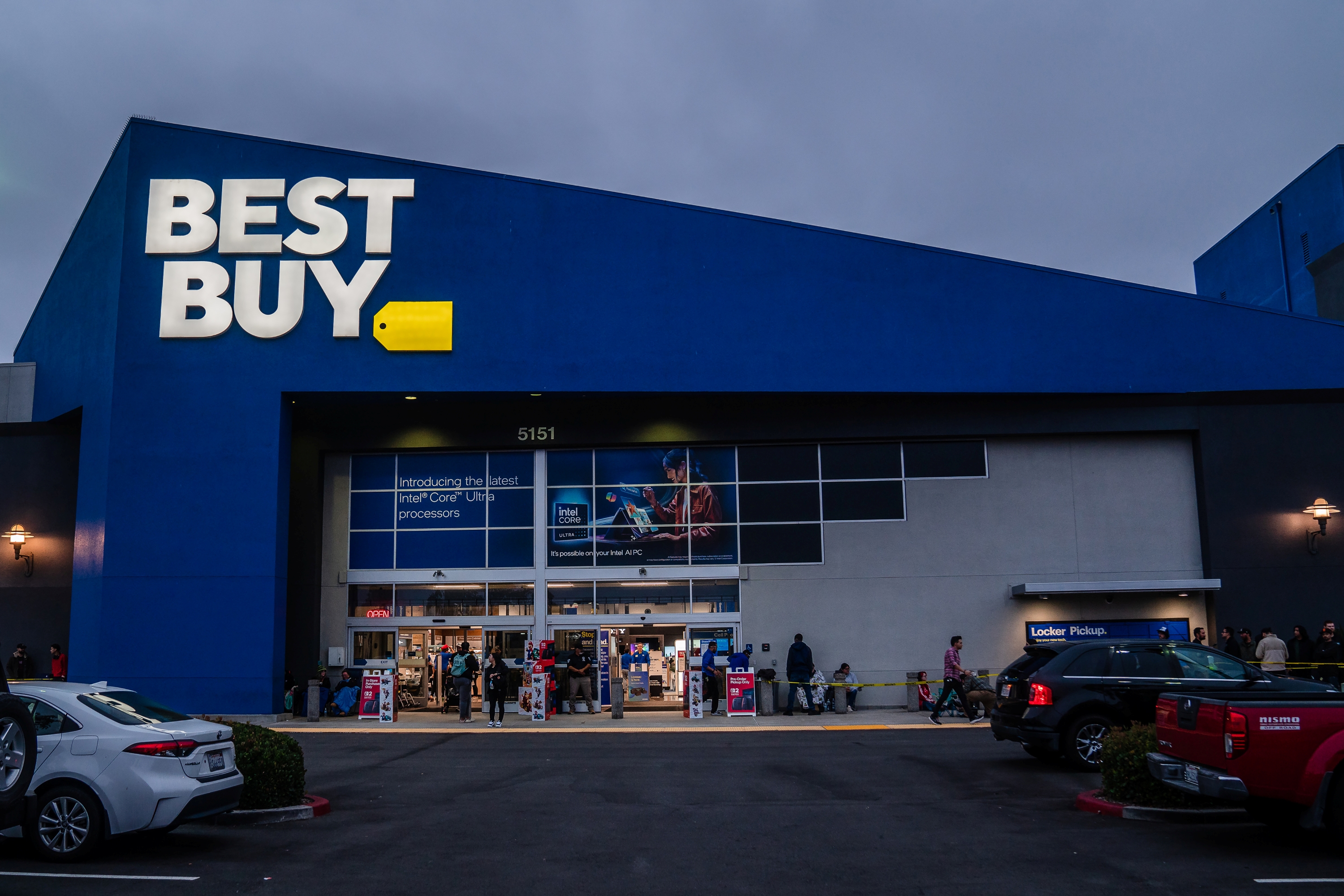 Exterior of a Best Buy store with a line of customers waiting outside