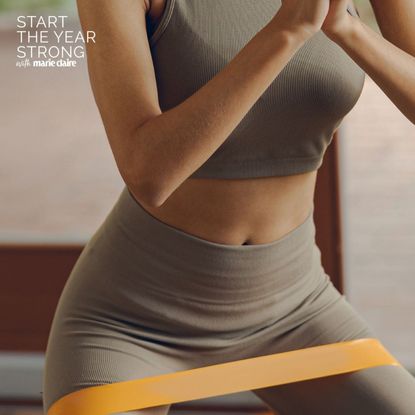 A woman doing a resistance band Pilates workout at home with headphones on