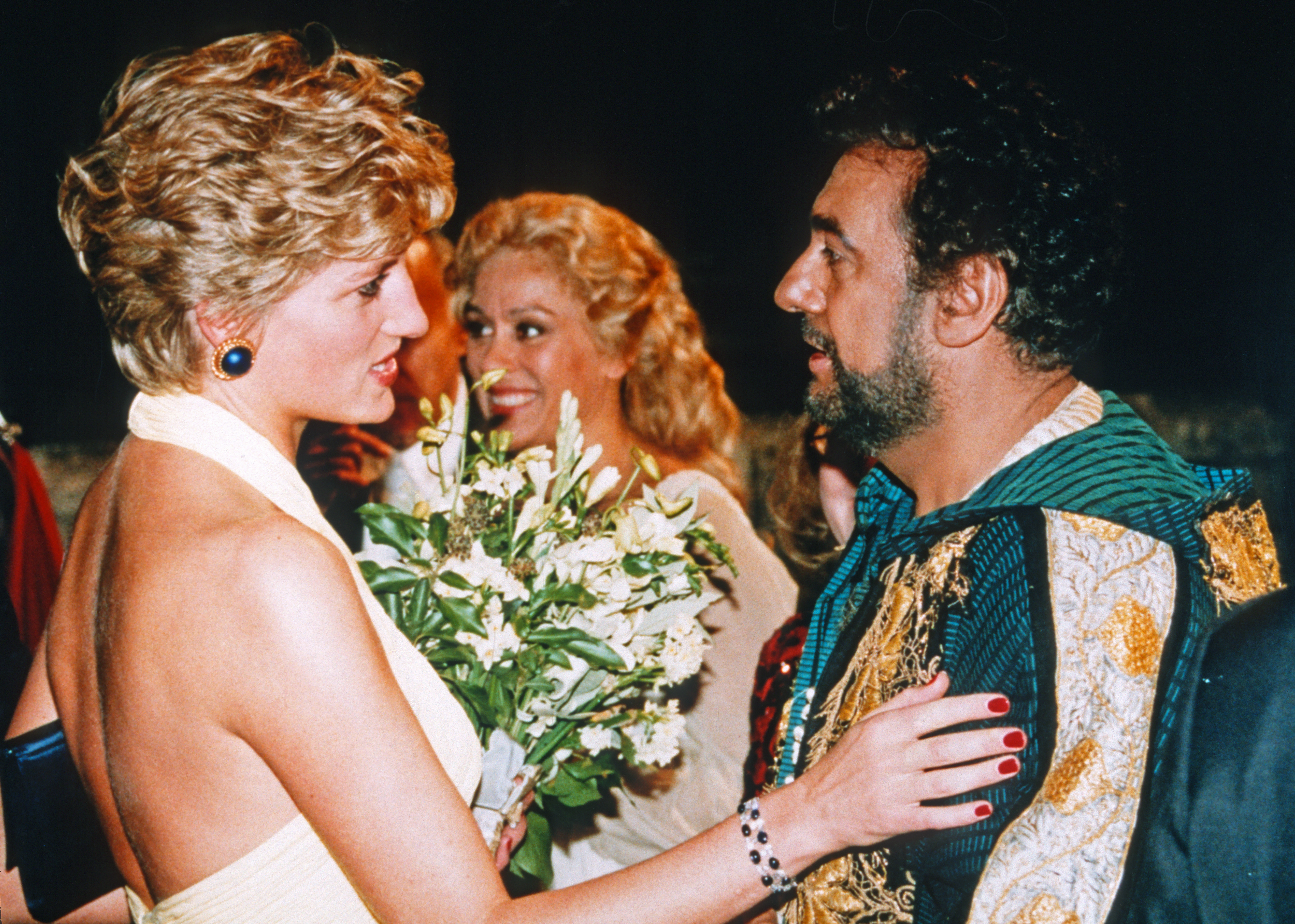 Princess Diana wearing a white dress talking to Placido Domingo and holding a bouquet of flowers in 1992