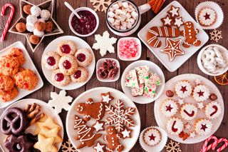 A wooden table filled with various sweet, festive snacks such as gingerbread men, Christmas cookies, and jam tarts.