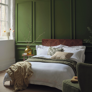 a green walled bedroom with large double bed dressed with white duvet and green throw