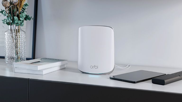 The Netgear Wi-Fi 6 Orbi RBK353 mesh network router shown on table next to books and a glass jar holding flowers