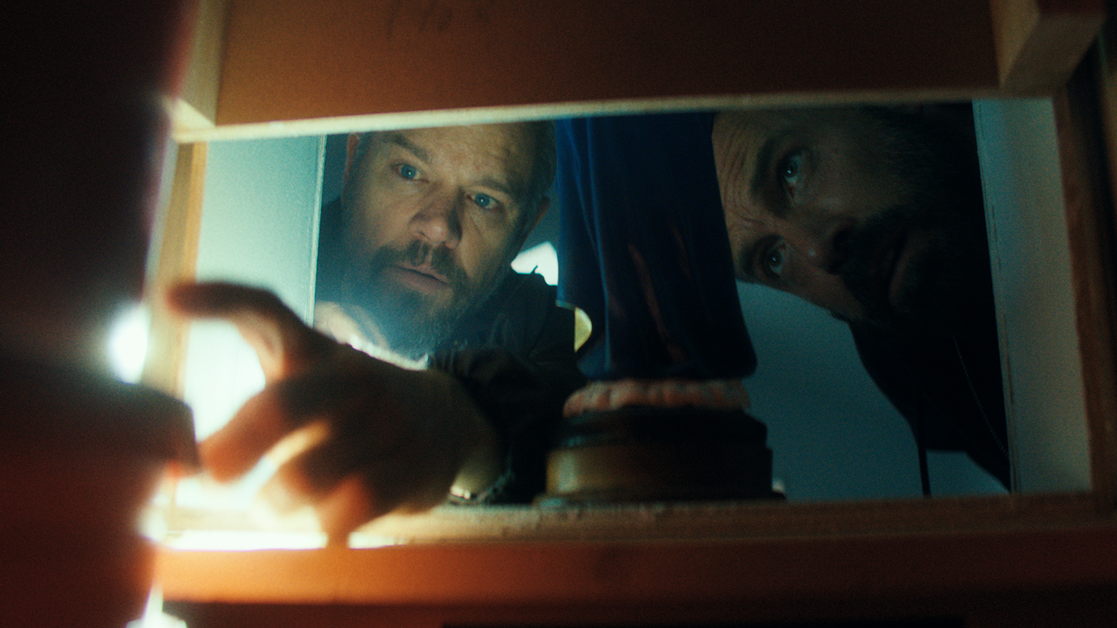 Dane shining a flashlight behind a secret gap in an attic hall as J.D looks on in The RIP