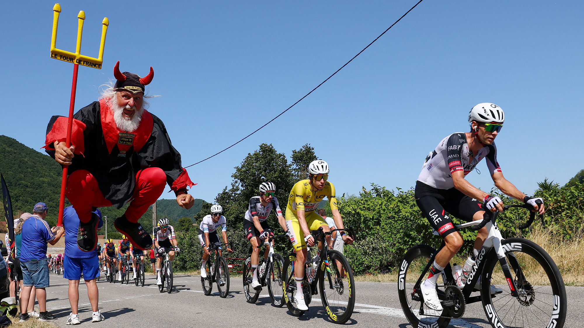 Costumed superfan Didi Senft leaps into the air as Isaac Del Toro and Tadej Pogačar of UAE Team Emirates-XRG pass by during Stage 17 of the Tour de France near Chambery, France