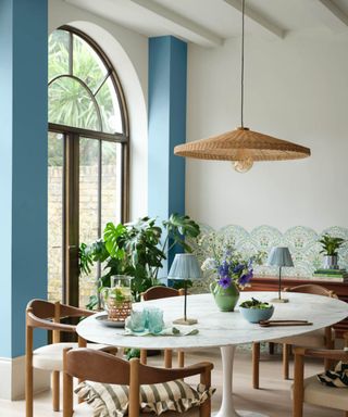 Dining room with arched window, round white dining table, rattan pendant light, plants and wooden dining chairs