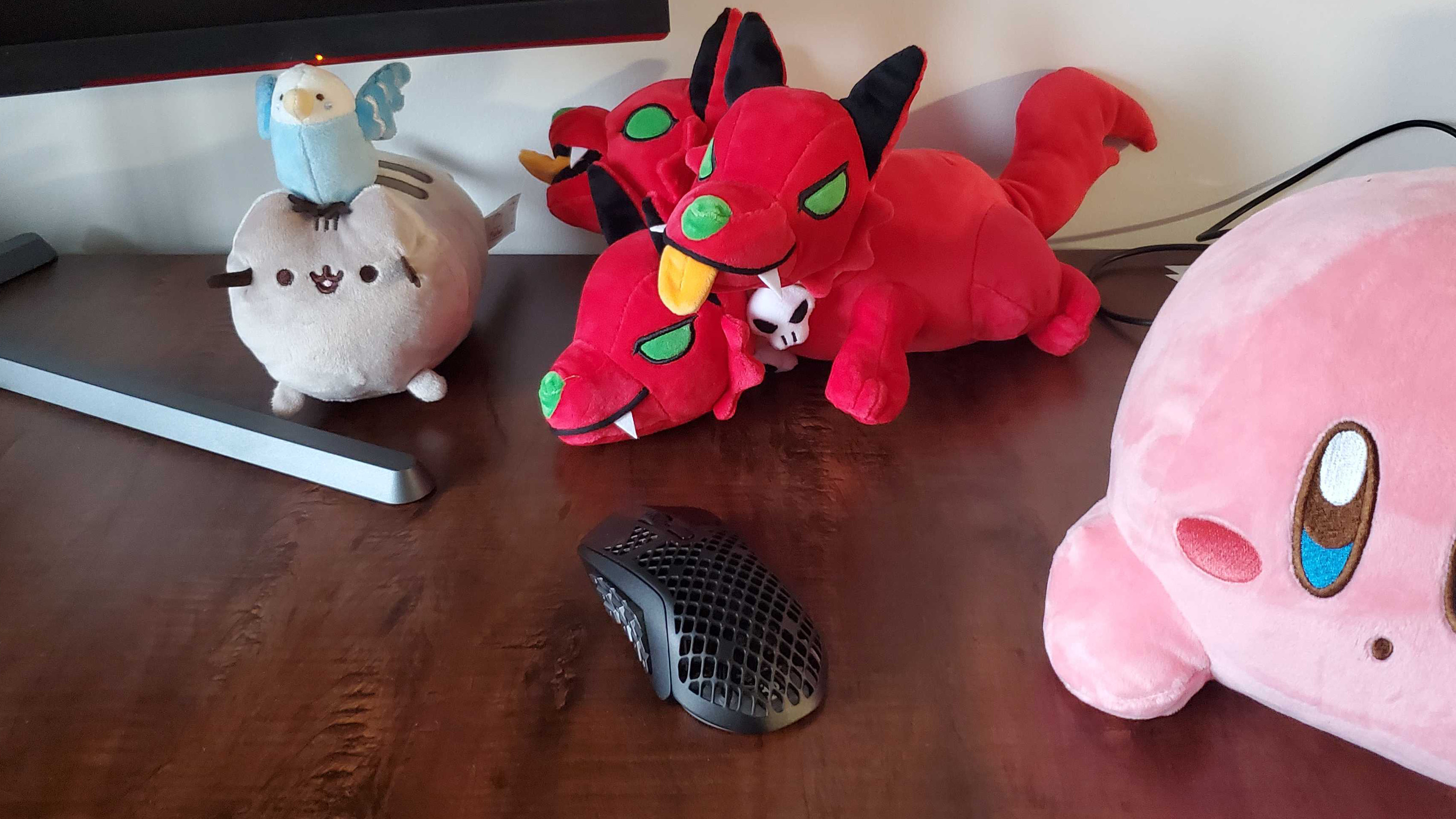 SteelSeries Aerox 9 on a dark wood desk next to some plushies