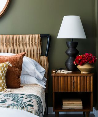 dark sage green bedroom with woven bed frame, wooden nightstand and white lamp