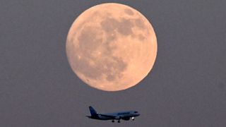 a large full moon shines at the top of the image with a passenger airplane flying below.